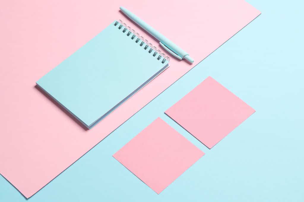 Un bloc-notes bleu, un stylo et des feuilles de papier rose disposés sur un fond bleu.